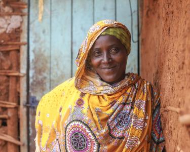 Madina Mohamed lebt in Isiolo County in Kenia, wo Oxfams Partnerorganisation MID-P die Wasserversorgung verbessert. Eine Frau lächelt in die Kamera. Sie lehnt an einer Wand, ihr Blick ist selbstsicher und stolz.