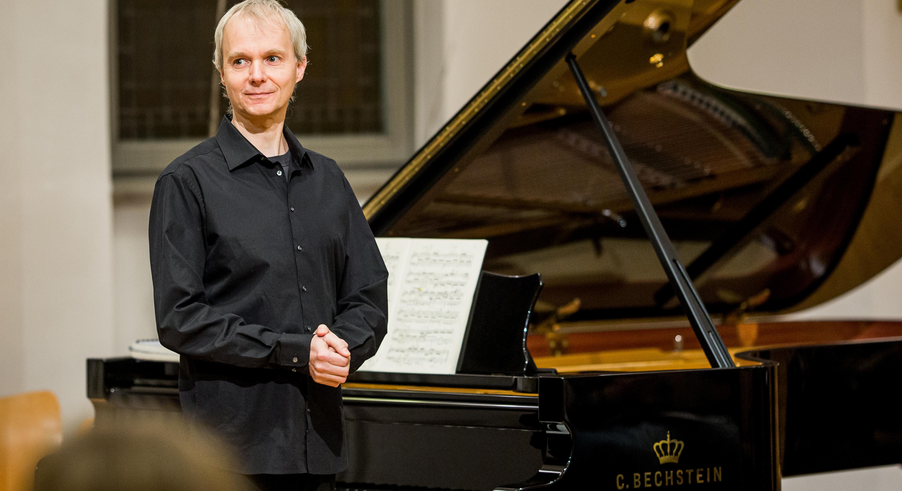 Ein Mann steht auf einer Bühne vor einem Flügel.