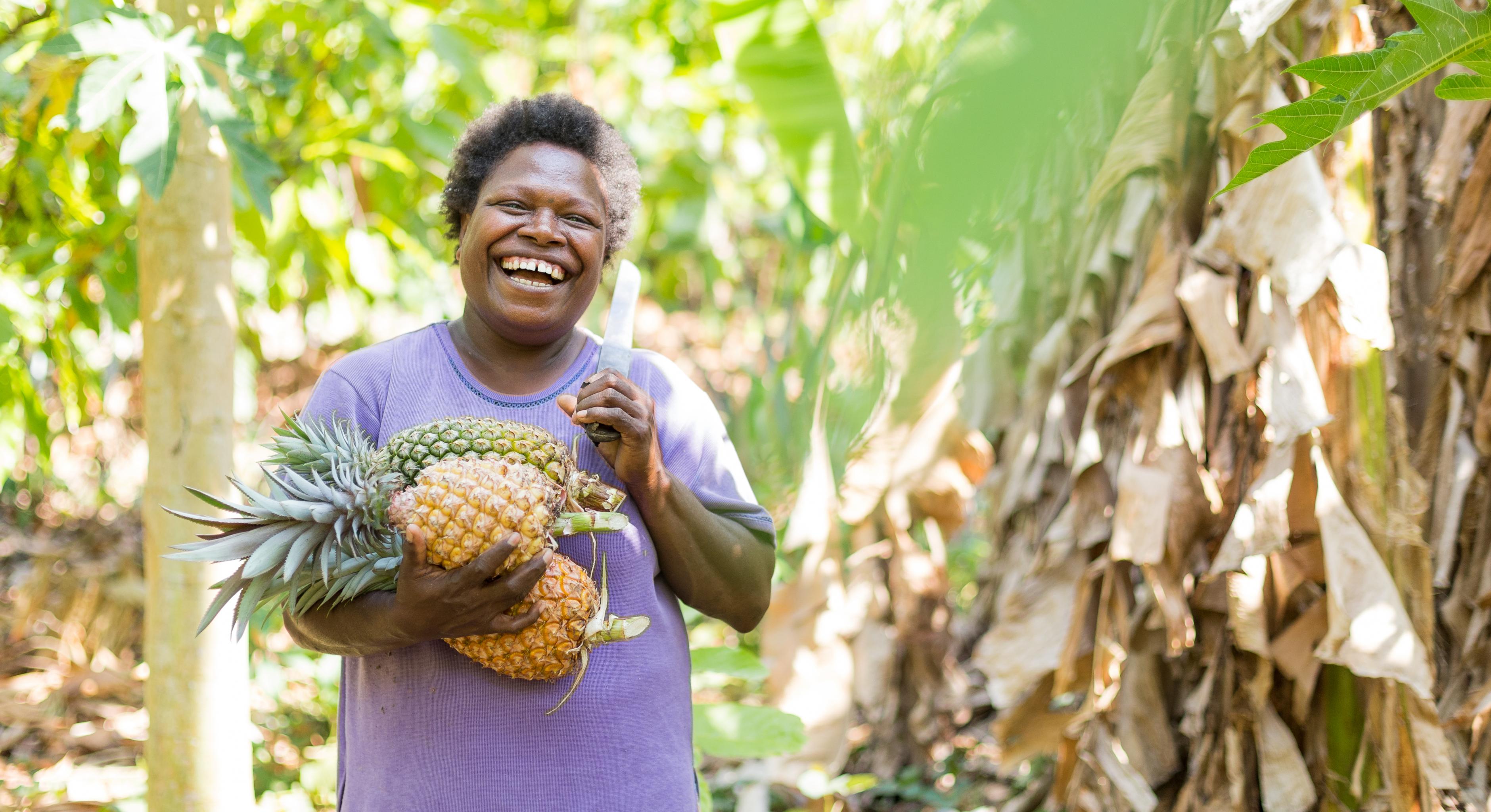 Eine lachende Frau mit Machete trägt Ananas