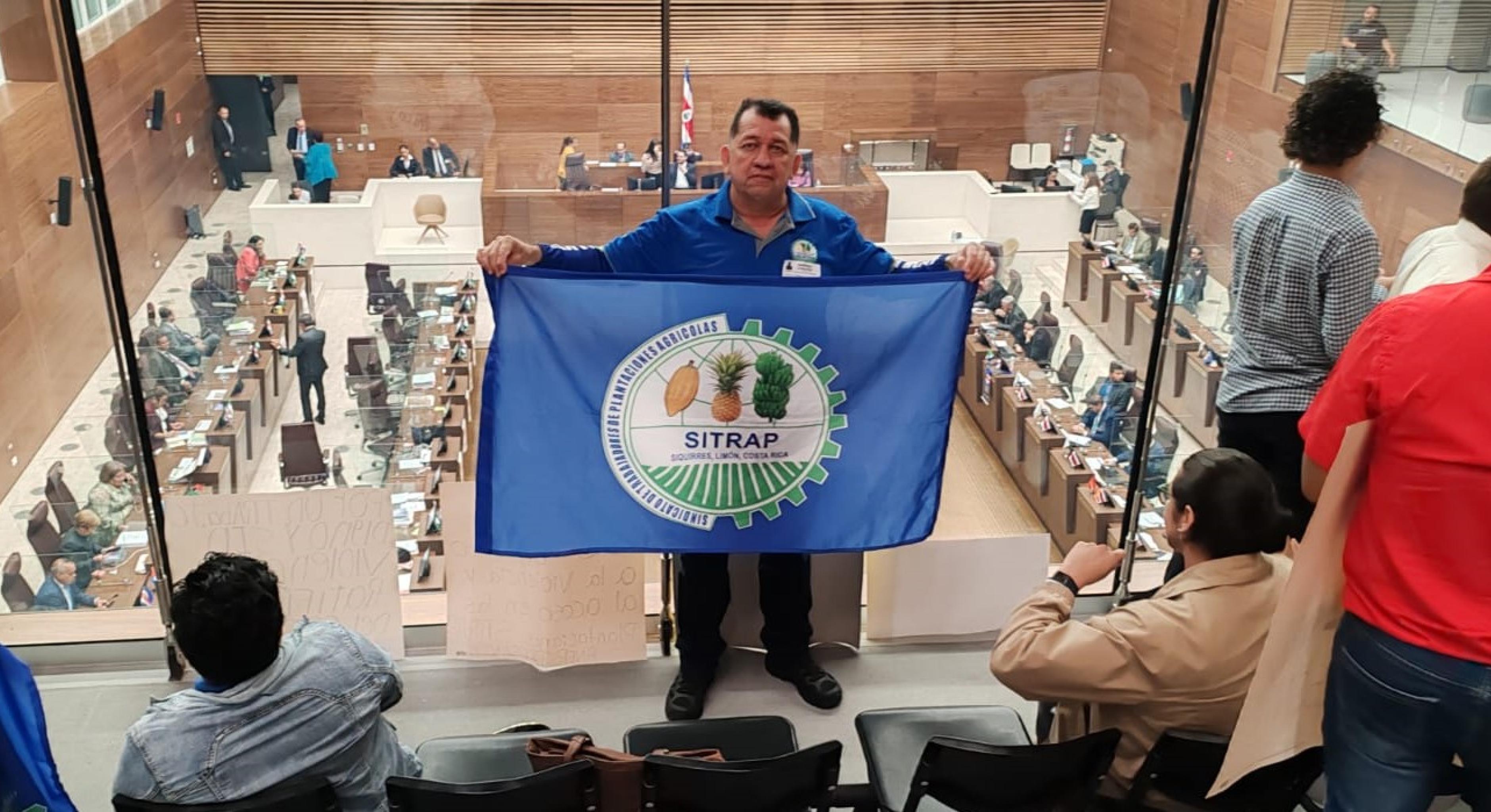 Gewerkschafter Didier Leitón steht in einer costa-ricanischen Institution und hält die Flagge seiner Gewerkschaft hoch.