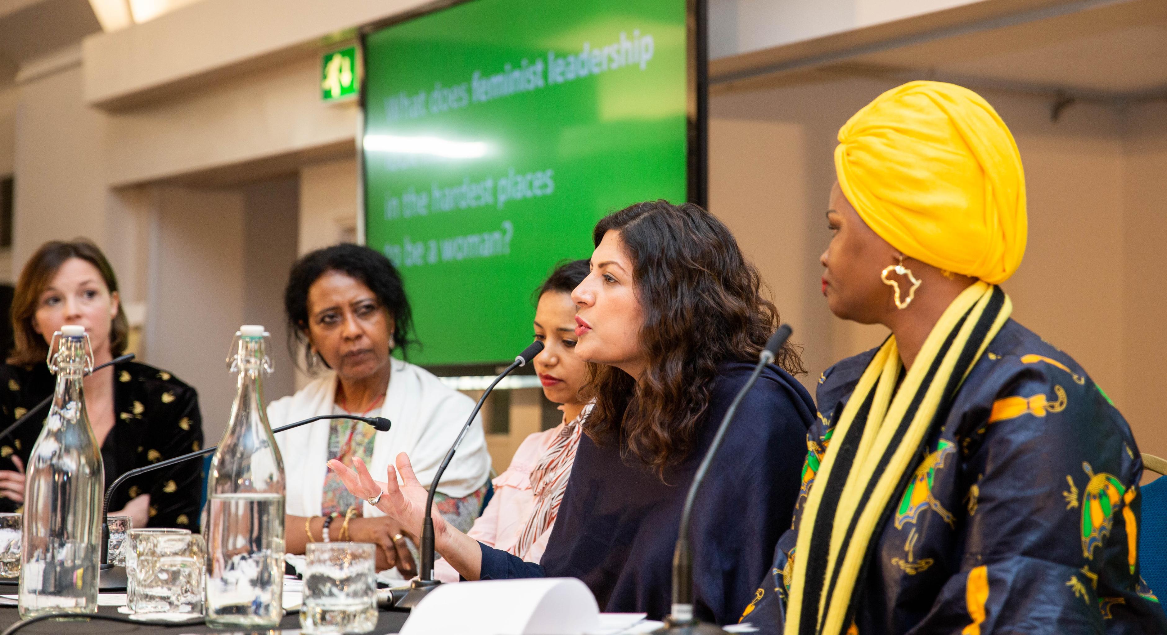Annie Kelly, Hala Al Karib, Rasha Obaid, Preet Kaur Gill MP und Riya William Yuyada sitzen an einem Tisch mit Tischmikrophonen und tauschen sich vor einem Publikum aus