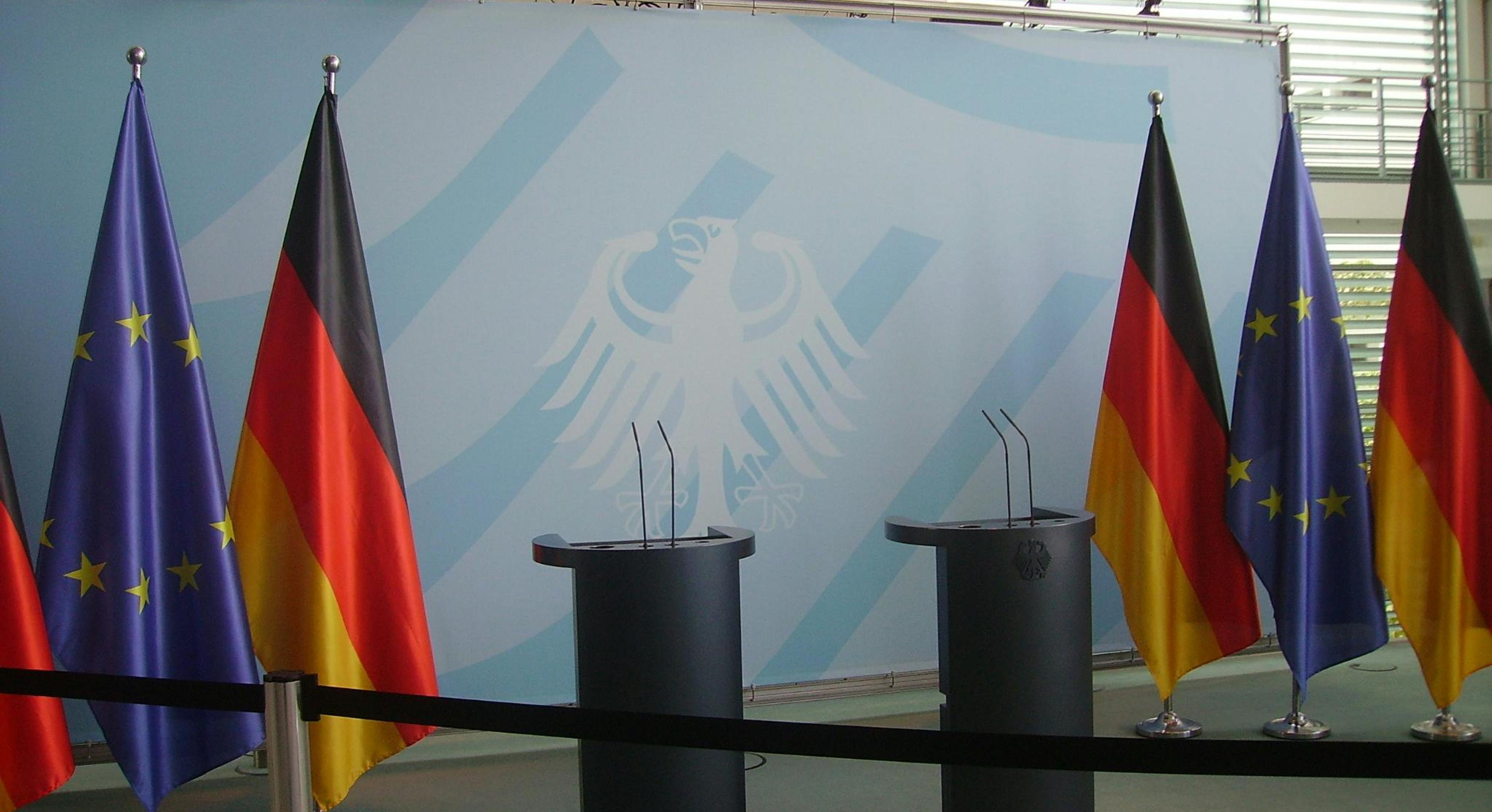 Flaggen der Europäischen Union und der Bundesrepublik Deutschland hängen neben zwei mikrofonierten Redepulten