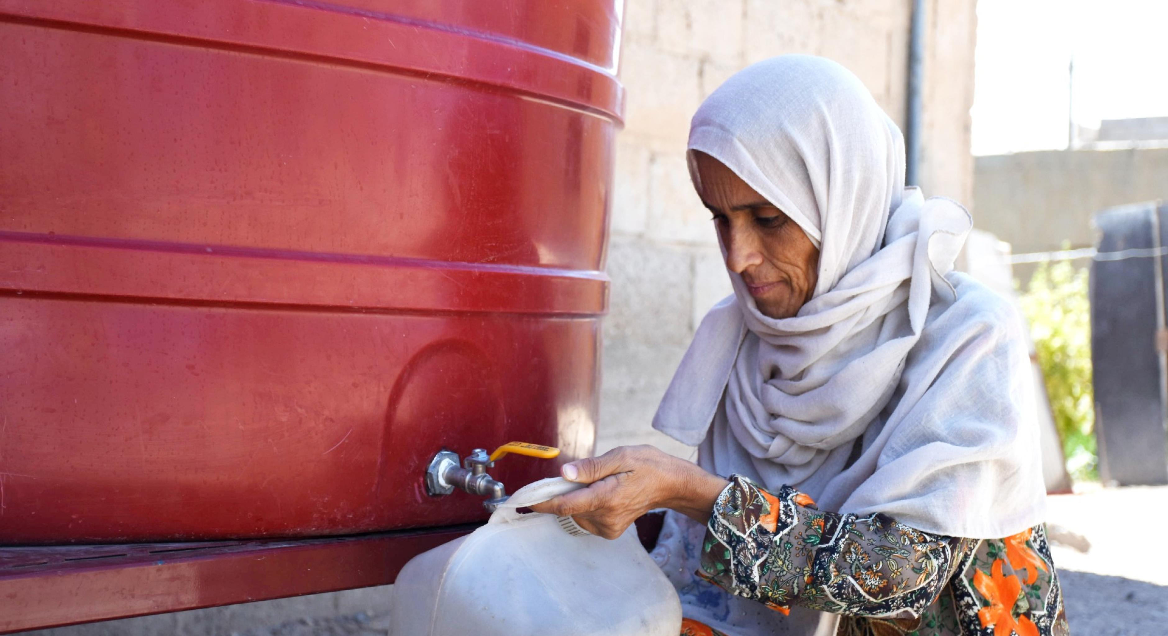 Eine syrische Frau aus Deir Ez-Zor füllt ihren Kanister mit Wasser aus einem Gemeinschaftstank.