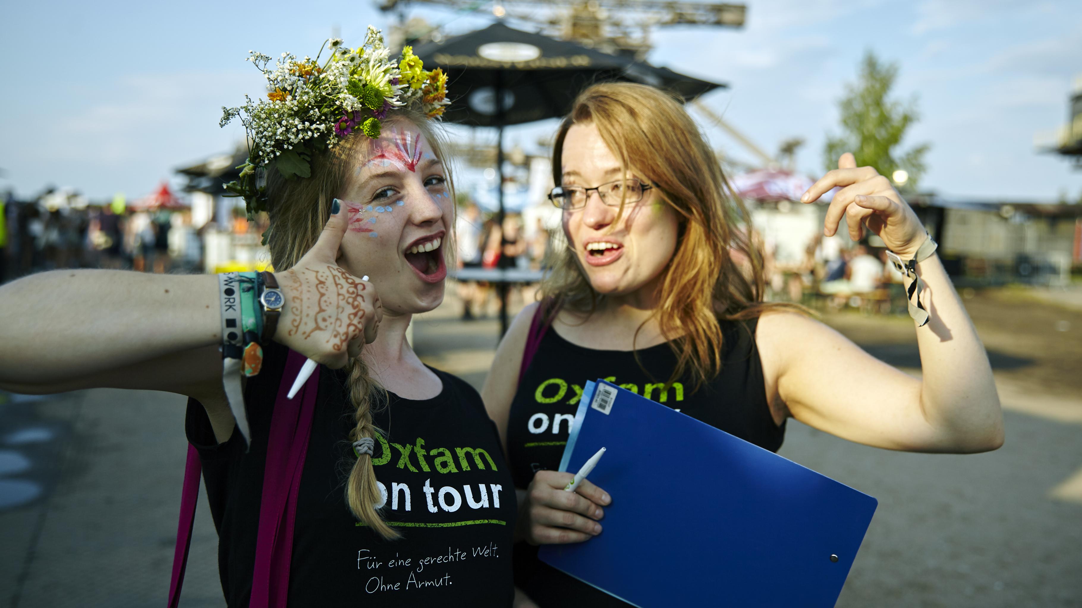 Zwei Konzertaktivistinnen mit einem mit Oxfam on Tour bedrucktem T-Shirt vor dem Hintergrund des Melt-Festivals
