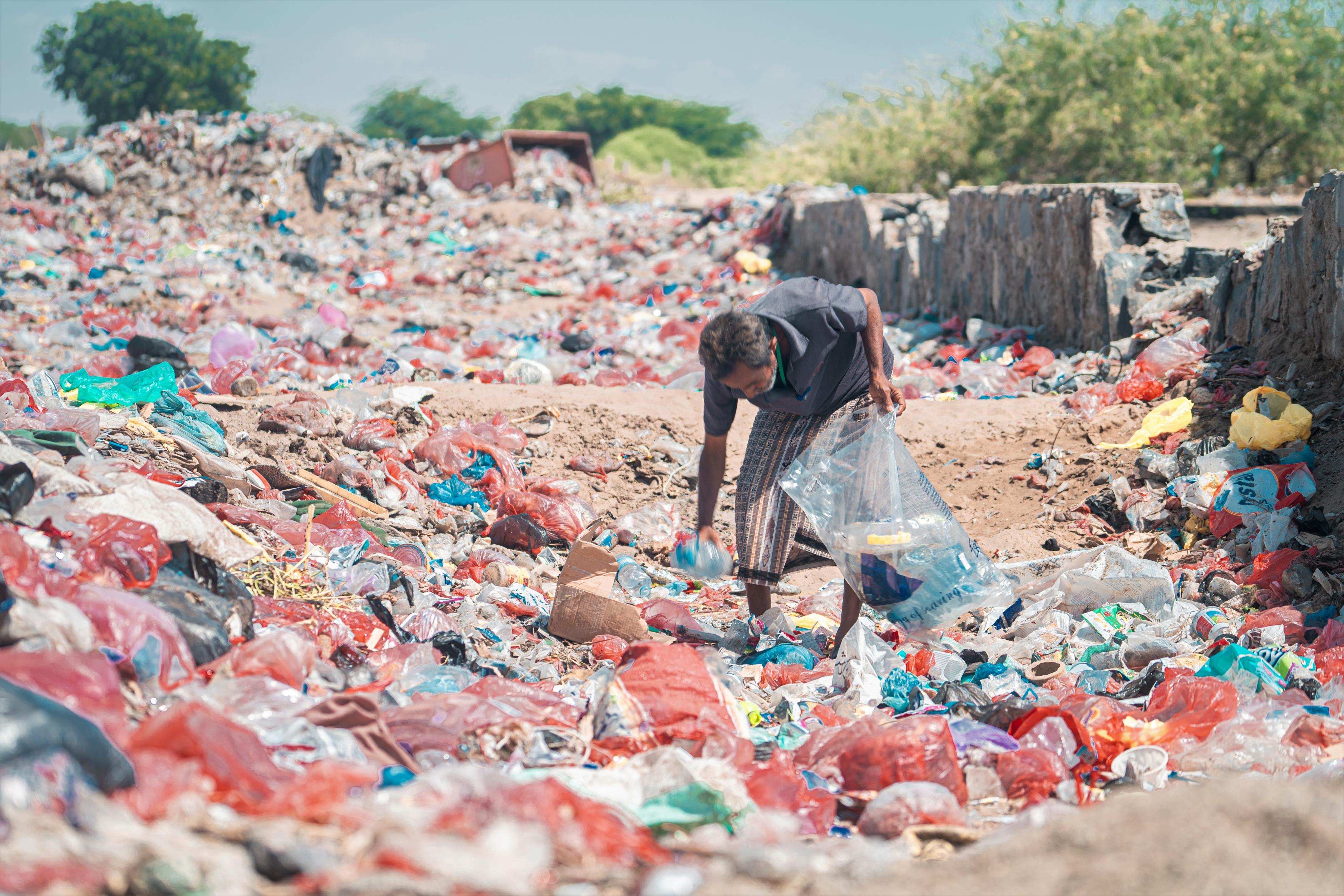 Khalid*, bekleidet mit einem dunkelgrauen T-Shirt und einer hellen, gemusterten Hose, sammelt leere Plastikflaschen aus einem Berg von Plastikmüll.