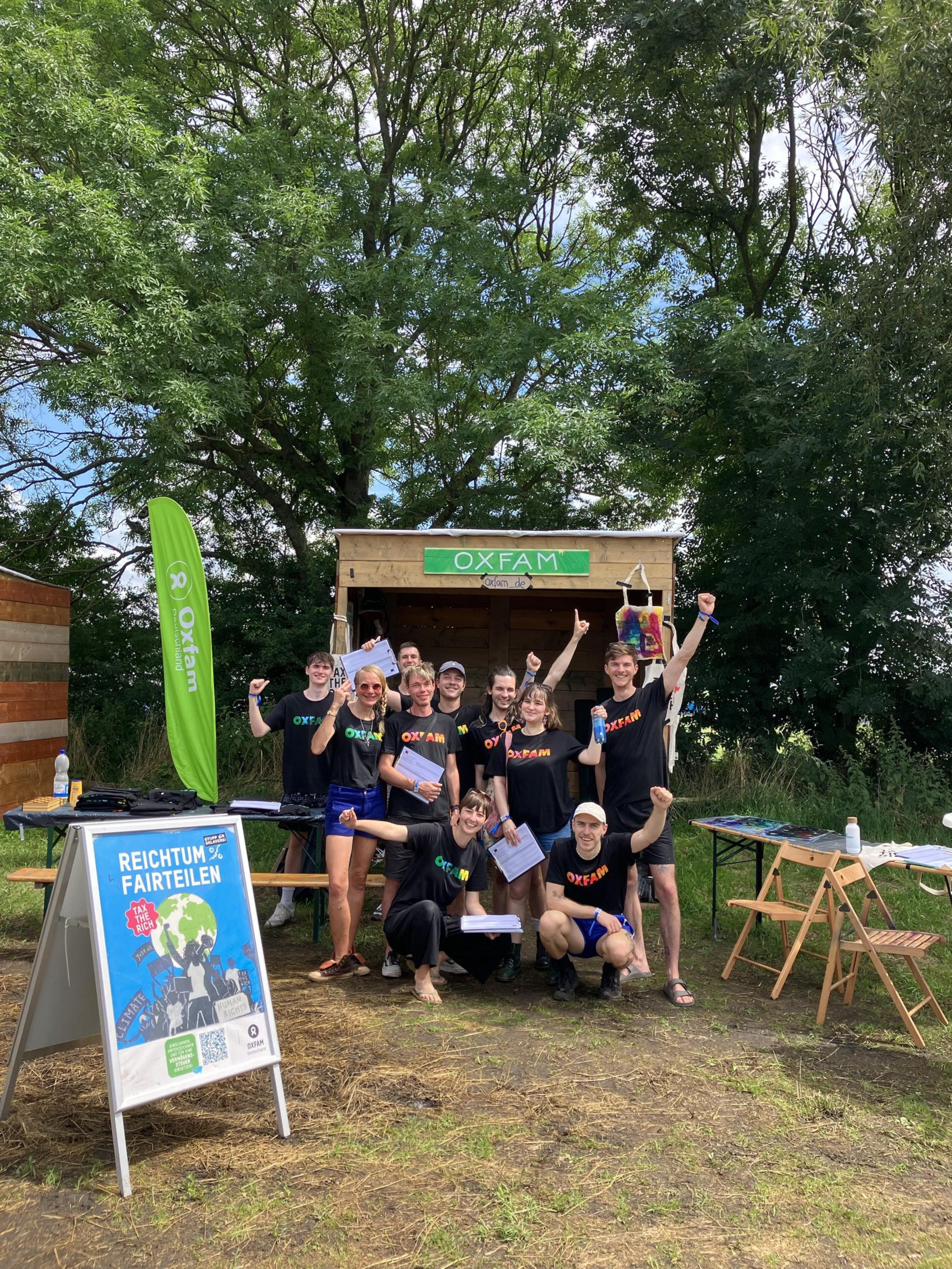 Eine Gruppe von Oxfam-Aktiven posiert mit Unterschriftenlisten vor dem Oxfam-Stand auf einem Festival