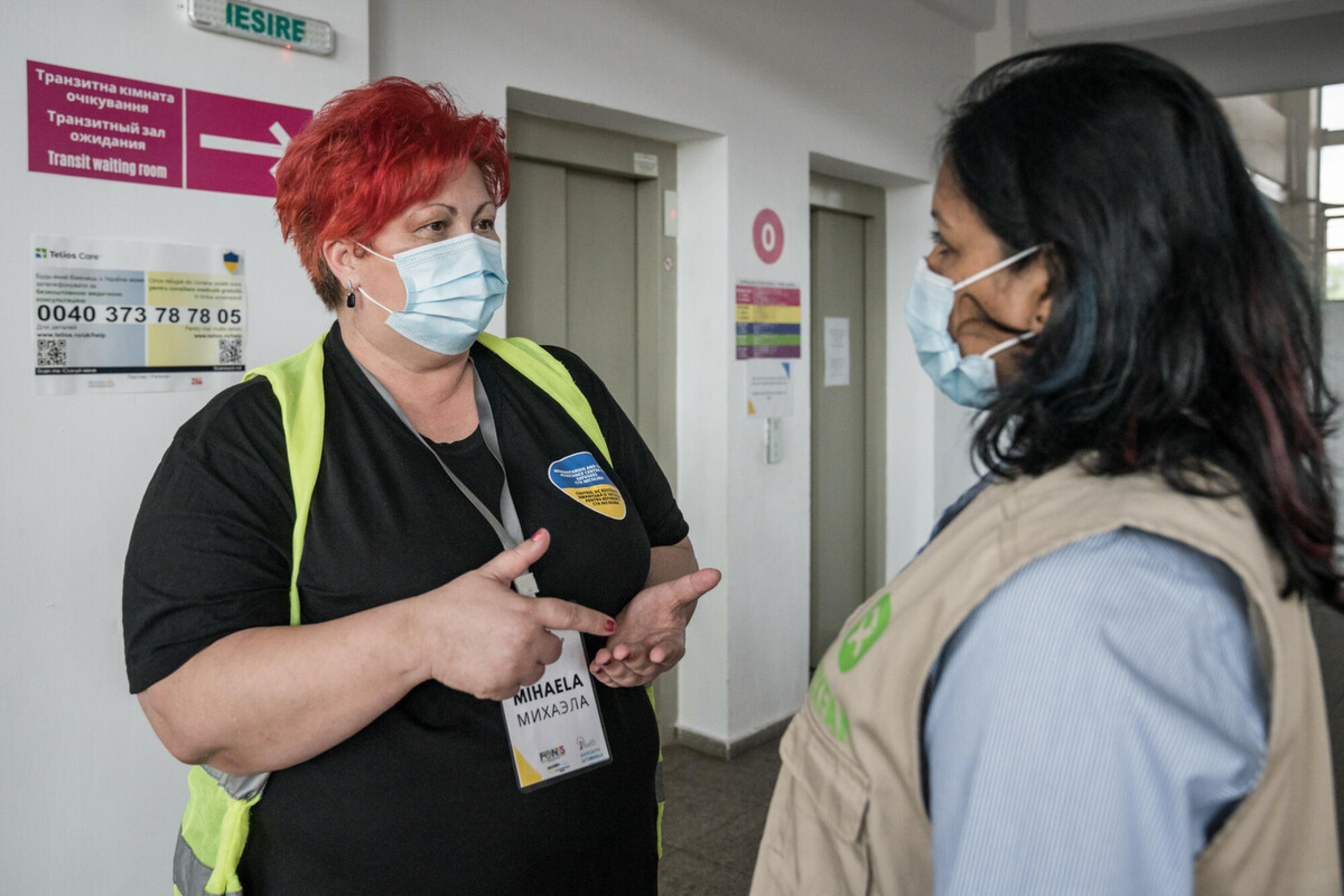 Die zwei Frauen Khodeza Akhtar Jahan Rume und Mihaela Olteanu unterhalten sich in einem Flur. Sie tragen medizinische Masken.