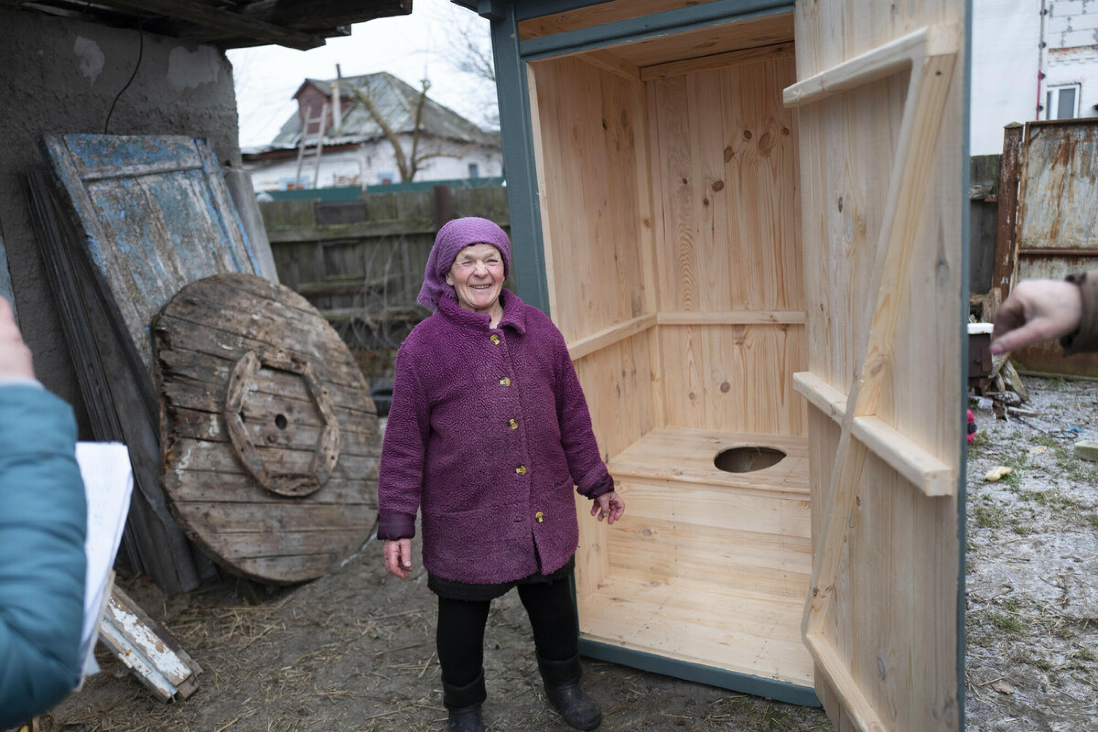 Nadiya Pavlenko steht vor ihrer neuen Latrine aus Holz. Sie strahlt in die Kamera.
