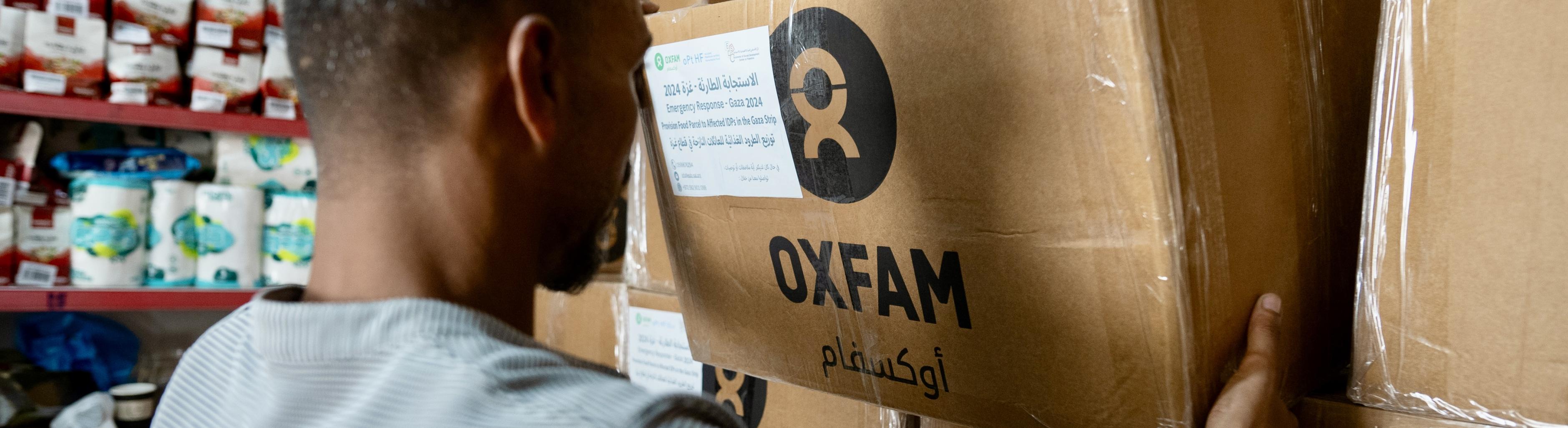 Ein Mensch hebt eine Oxfam-Kiste mit Hilfsgütern von einem Stapel