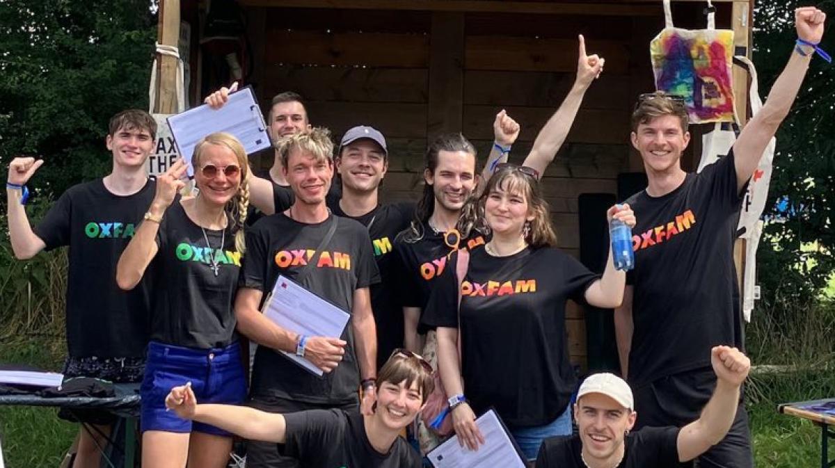 Eine Gruppe von Oxfam-Aktiven posiert mit Unterschriftenlisten vor dem Oxfam-Stand auf einem Festival