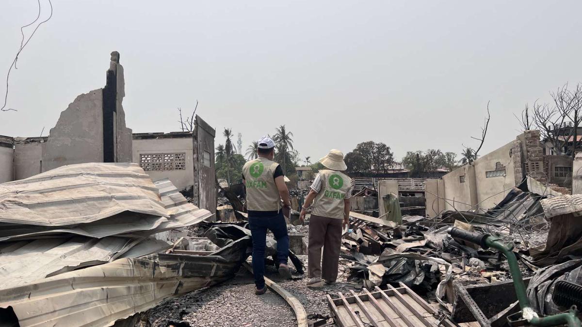 Zwei Personen in Oxfam-Westen stehen zwischen Trümmern.