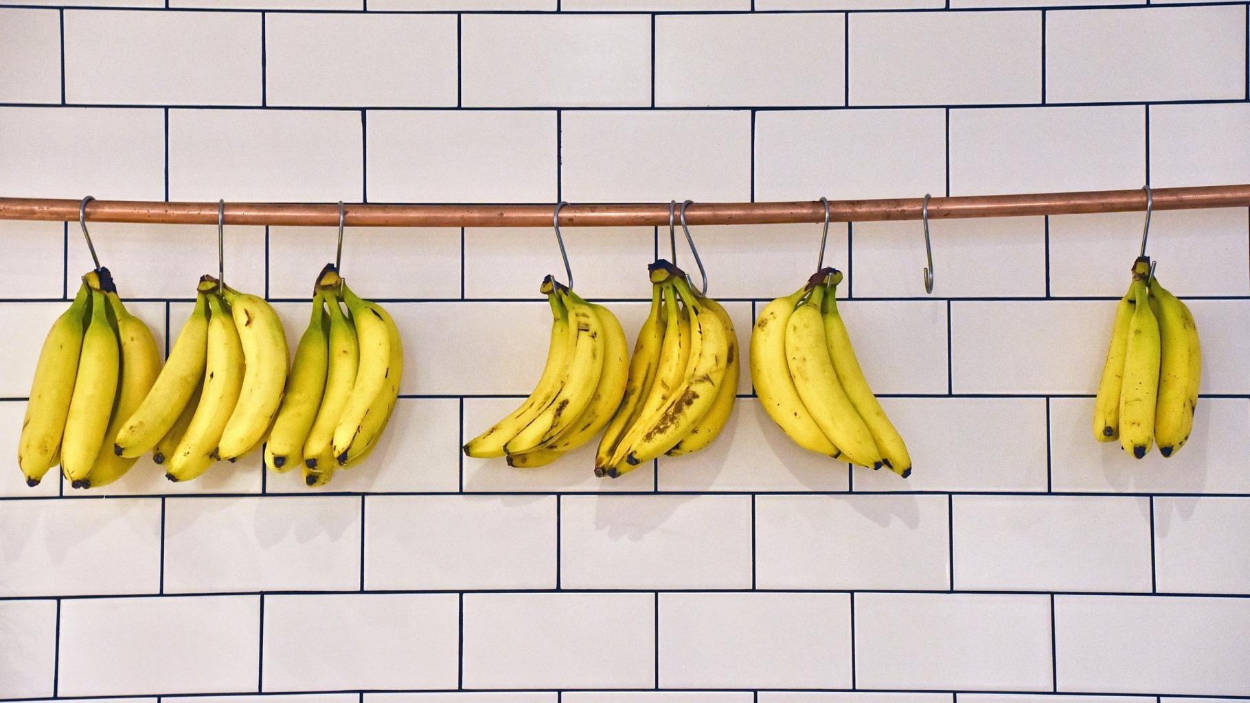 Bananenbündel, die an einer Stange vor einer gekachelten Wand hängen