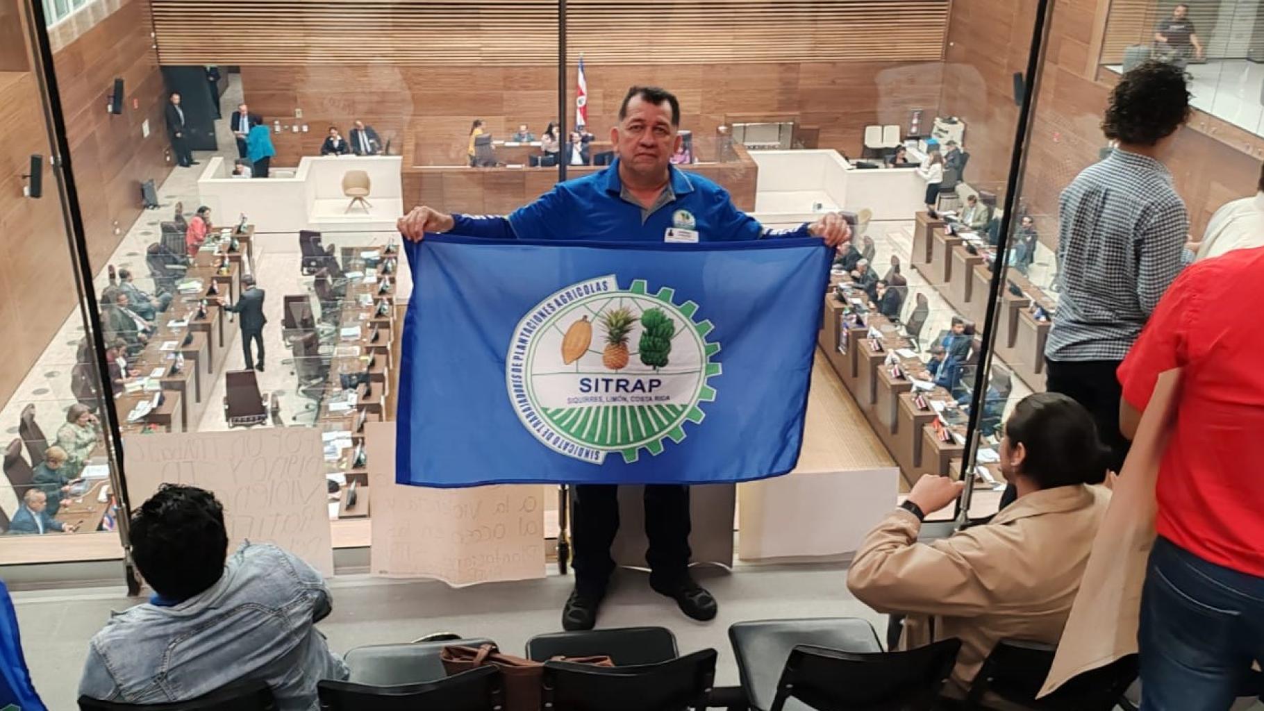 Gewerkschafter Didier Leitón steht in einer costa-ricanischen Institution und hält die Flagge seiner Gewerkschaft hoch.