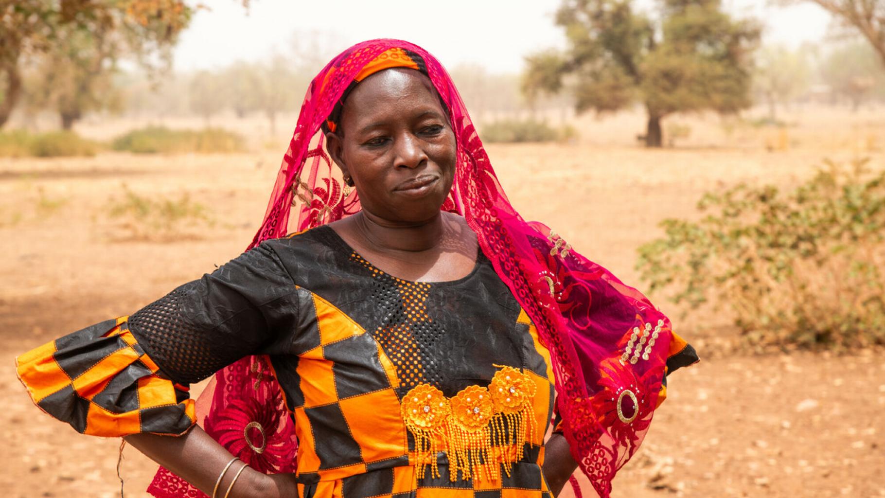 Sanfo Ramata ist Bäuerin und Viehzüchterin. Sie arbeitet für die Confédération Paysanne du Faso, eine Partnerorganisation von Oxfam. Die Frau steht in einem bunten Kleid vor einem Haus. Sie sieht nachdenklich aus.