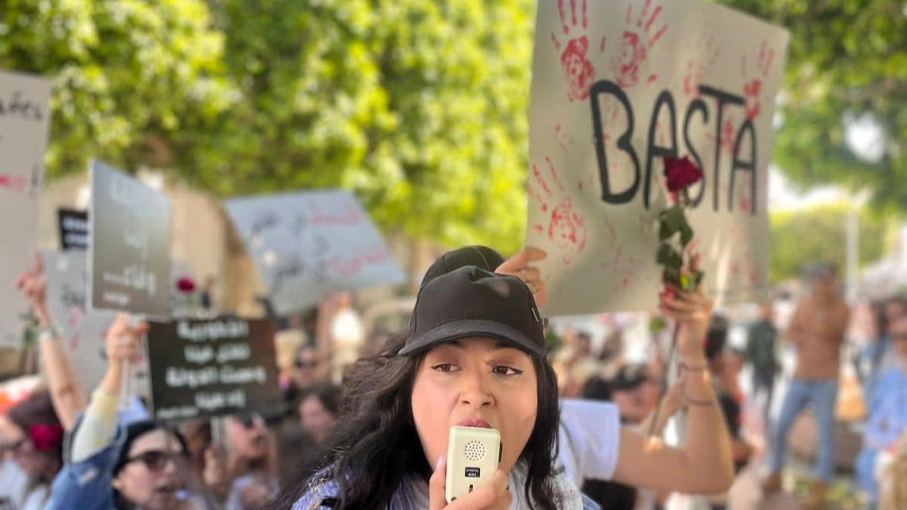 Rahma Idoudi, eine Mitarbeiterin von Aswat Nissa, spricht auf einer Demo in Tunis in ein Megafon. Hinter ihr sind Demonstrant*innen mit Plakaten zu sehen.
