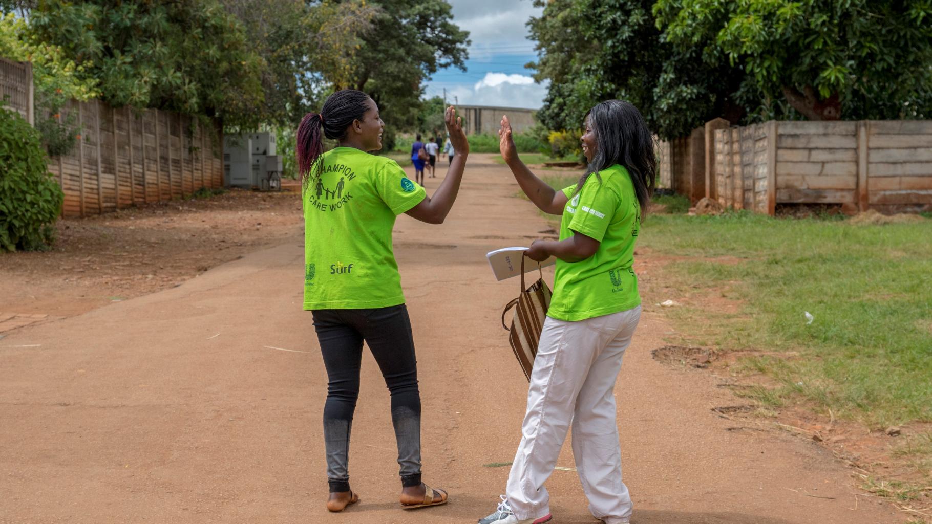 Abigail und Shylet geben sich ein High-Five auf dem Weg nachhause. Sie tragen grüne T-Shirts mit der Aufschrift "Champions-Care Work"