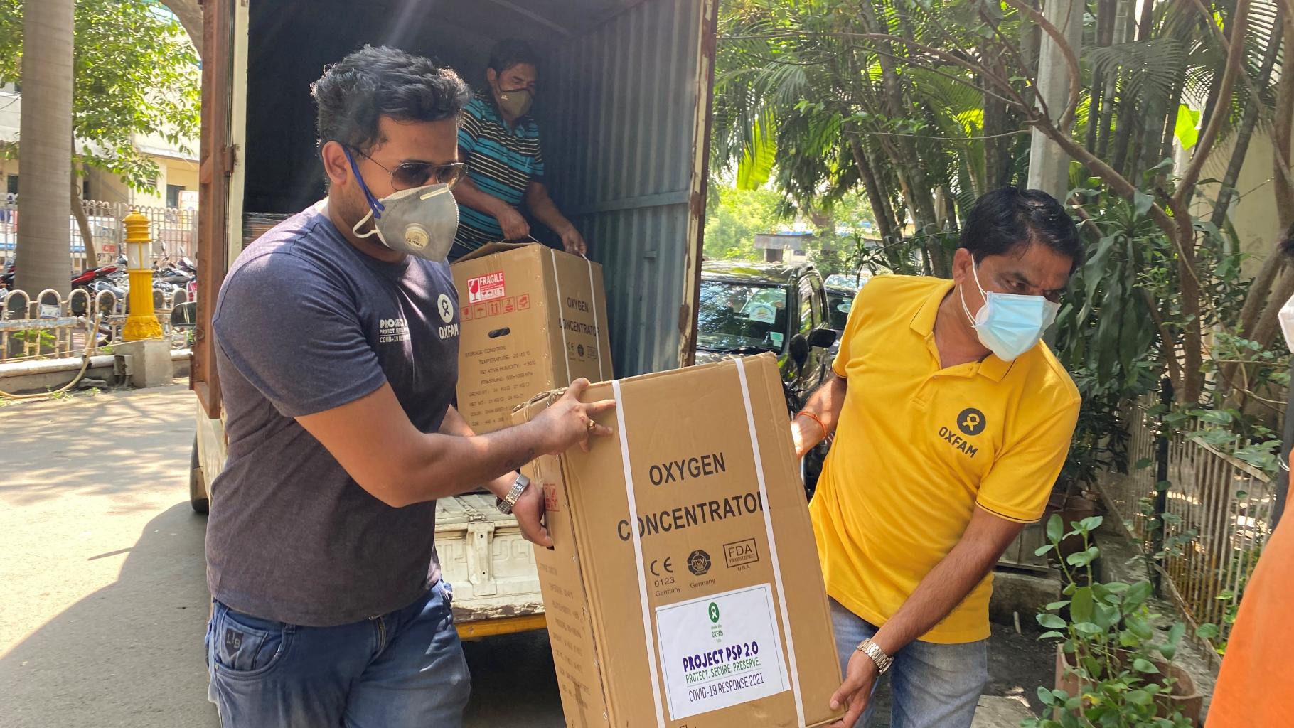 Zwei Mitarbeiter von Oxfam Indien tragen einen Karton mit einem Sauerstoffkonzentrator.