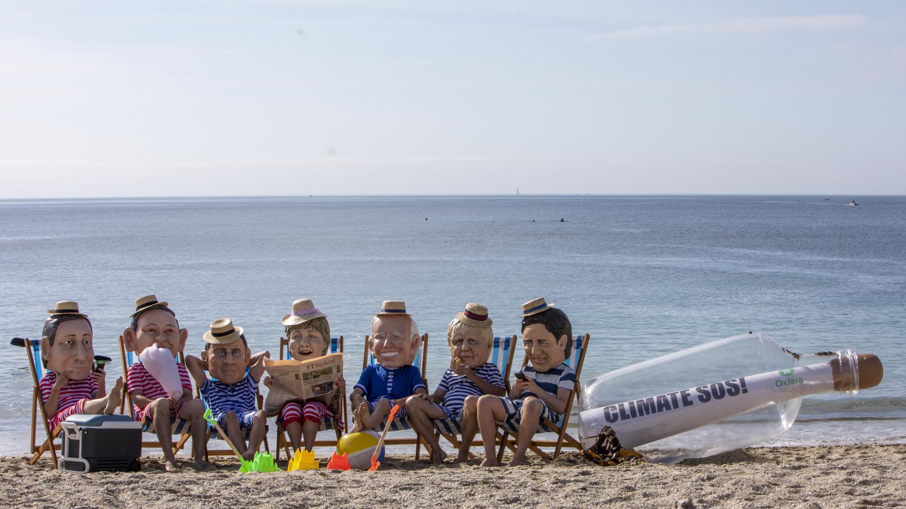Aktivist*innen posieren als G7-Regierungschef*innen am Strand. Sie tragen gestreifte Badesachen und Sonnenhüte.