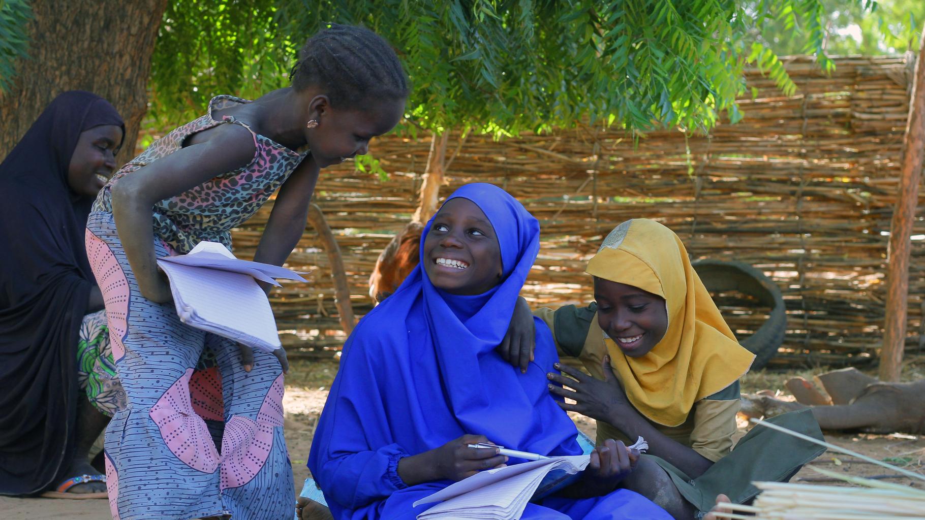 Drei Kinder sitzen auf dem Boden und schreiben in ihre Schulhefte