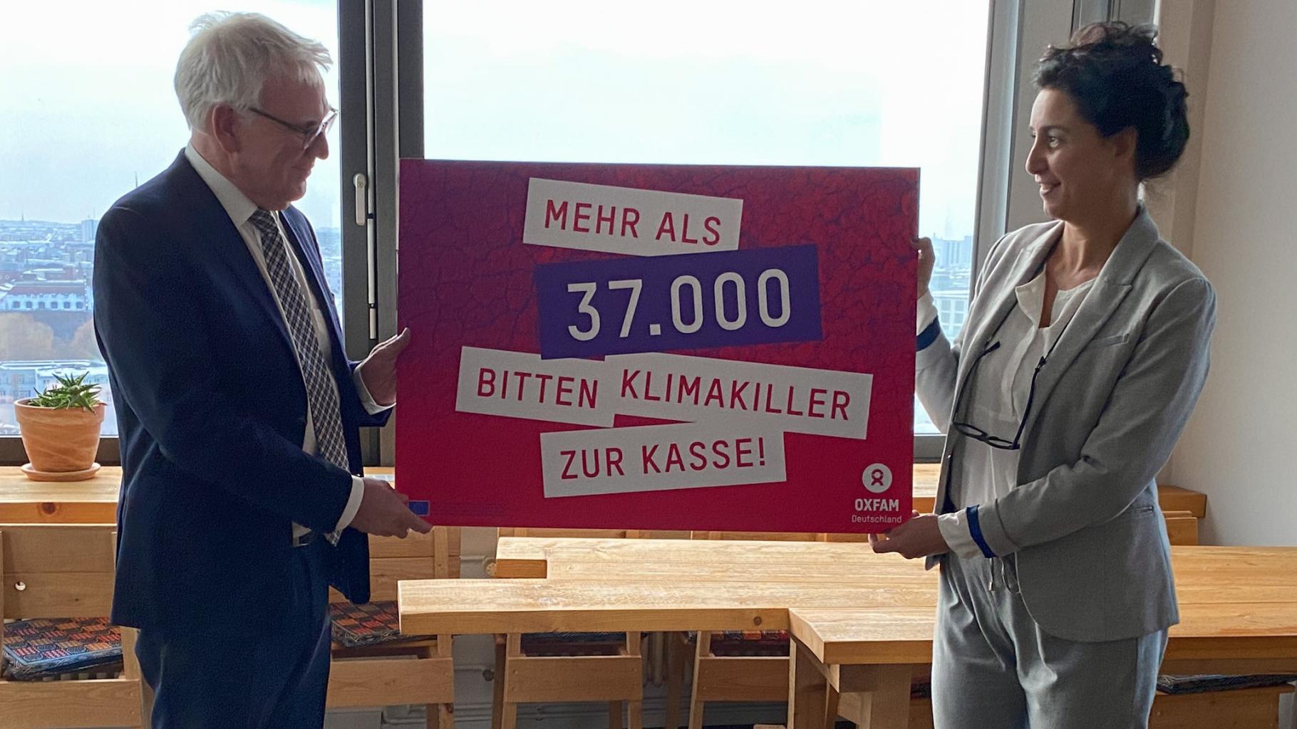 Zwei Menschen halten ein Schild hoch, auf dem steht: Mehr als 37.000 bitten Klimakiller zur Kasse. Dies bezieht sich auf eine Unterschriftenaktion, die Aufmerksamkeit auf eine gerechte Klimapolitik lenken soll.