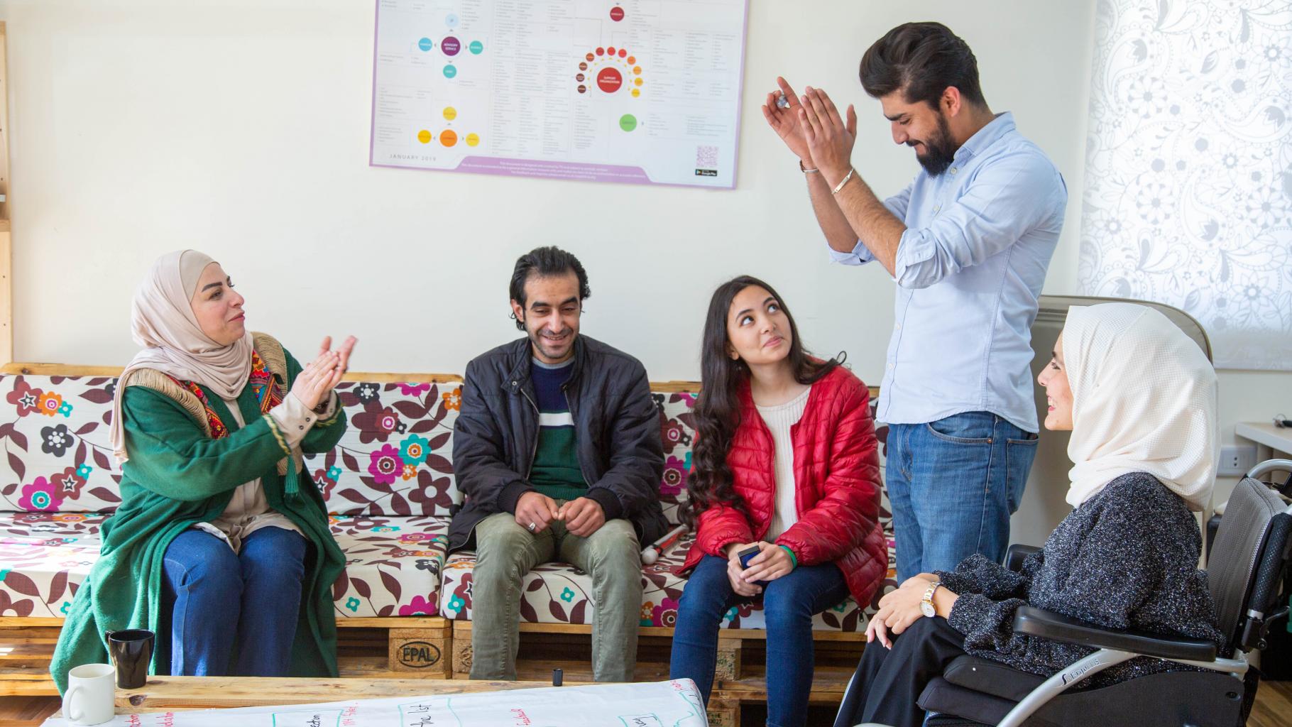 Hala, Rana, Abed und Mohammed sitzen in einem Kreis, ihr Geschäftspartner steht zwischen ihnen.
