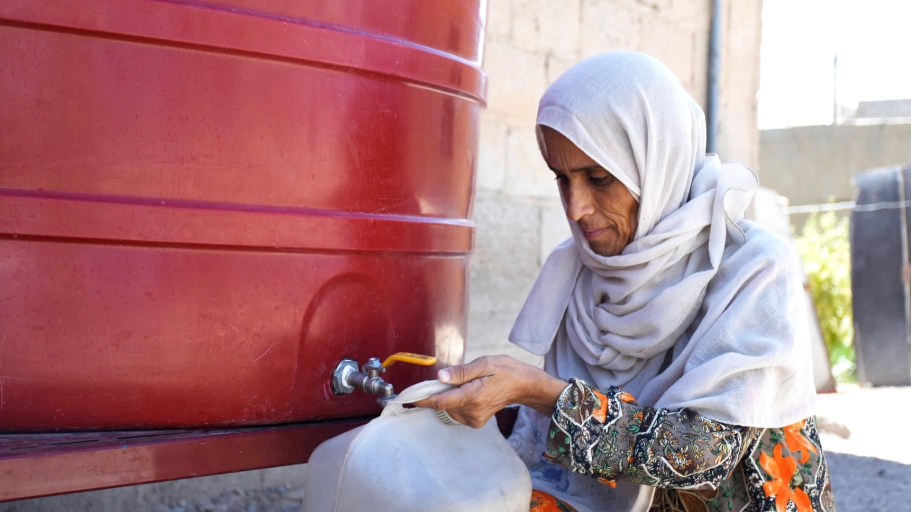 Eine syrische Frau aus Deir Ez-Zor füllt ihren Kanister mit Wasser aus einem Gemeinschaftstank.