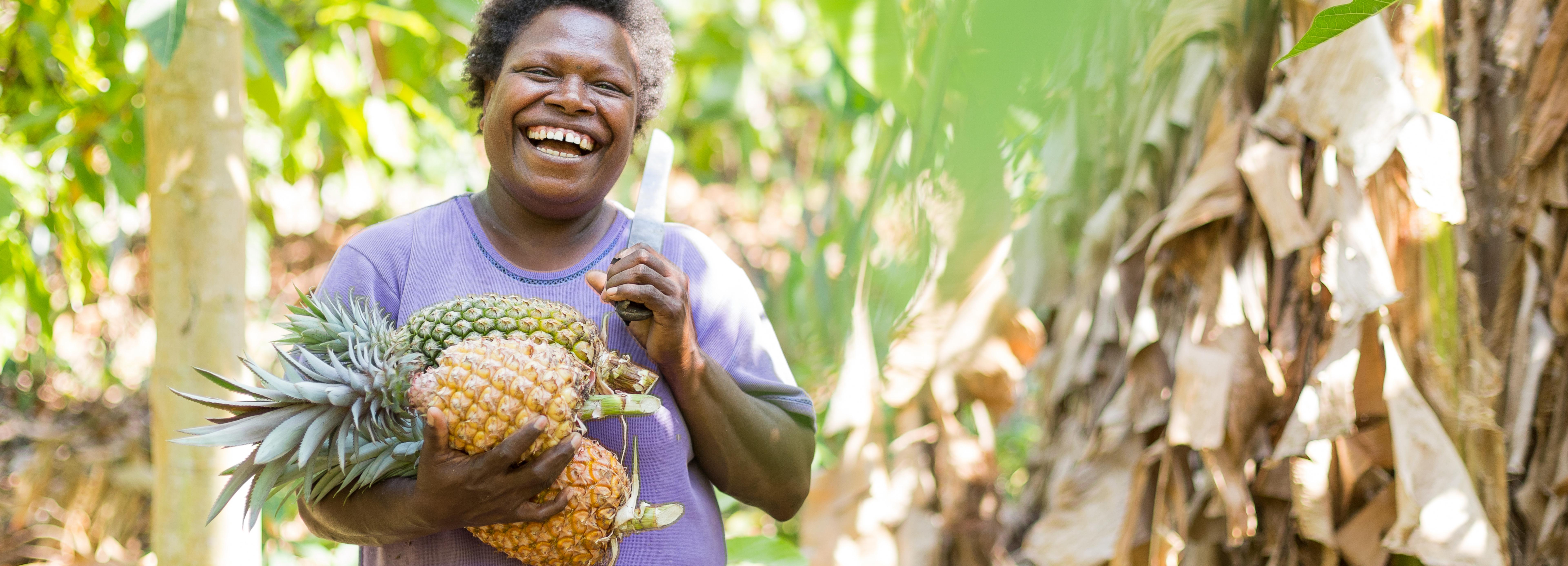 Eine lachende Frau mit Machete trägt Ananas