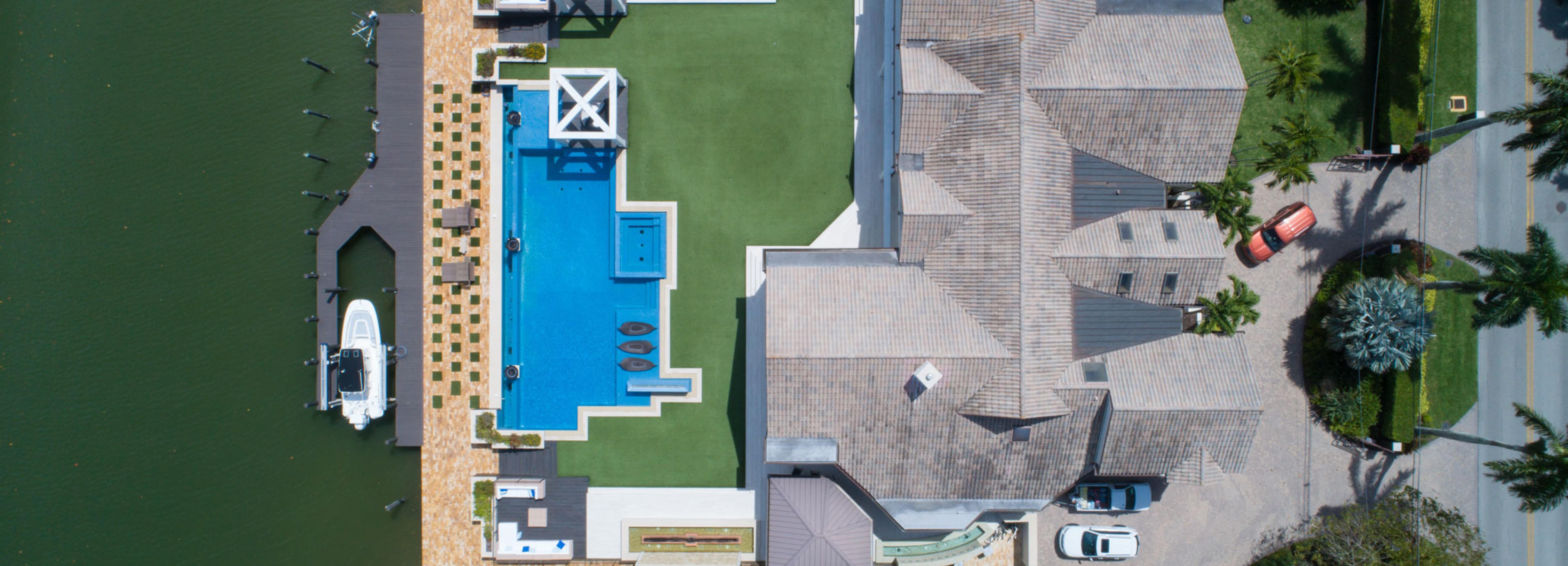 Luftaufnahme einer Villa mit Fuhrpark, Pool, Boot und Anlegestelle