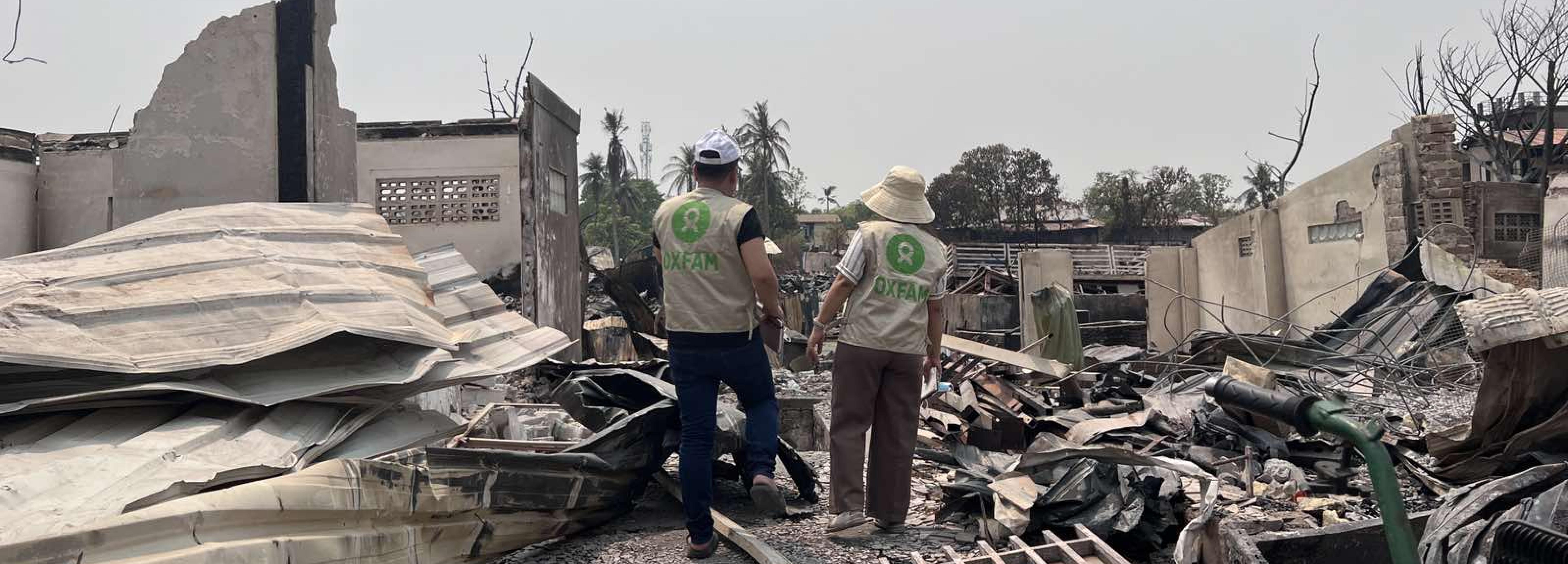 Zwei Personen in Oxfam-Westen stehen zwischen Trümmern.