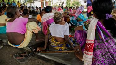 Frauen in bunten Saris sitzen im Halbkreis auf dem Boden und verfolgen einen Vortrag
