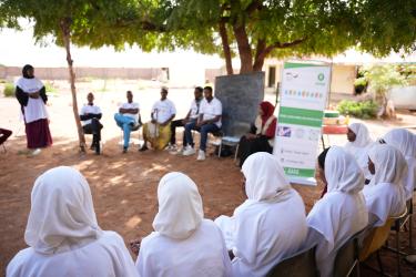 Geschlechtergerechtigkeit ist eines der vier Kernthemen von Oxfam. Eine Gemeinschaft sitzt im Schatten eines Baumes im Kreis und spricht über regelmäßiges Händewaschen. Dabei stehen Frauen im Vordergrund des Bildes.