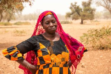 Klimakrise in Burkina Faso: Sanfo Ramata ist Bäuerin und Viehzüchterin. Sie arbeitet für die Confédération Paysanne du Faso, eine Partnerorganisation von Oxfam. Ihr Vieh stirbt wegen des Futtermangels und der Wasserknappheit, die durch die Klimakrise verstärkt werden. Sanfo Ramata ist Bäuerin und Viehzüchterin. Sie arbeitet für die Confédération Paysanne du Faso, eine Partnerorganisation von Oxfam. Die Frau steht in einem bunten Kleid vor einem Haus. Sie sieht nachdenklich aus.
