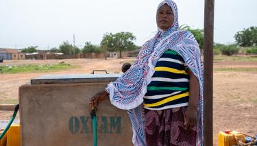 Eine Frau steht vor einem von Oxfam installierten Wassertank und dreht den Hahn auf.