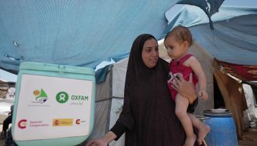Duaa Abu Sabha benutzt eine Handwaschstation, die Oxfam für Geflüchtete im Gebiet Al-Mawasi im Gouvernement Khan Yunis aufgestellt hat. Duaa Abu Sabha wäscht sich die Hände an einer Handwaschstation, die in einem Camp für Geflüchtete steht. Auf dem Arm trägt sie ein Kleinkind.