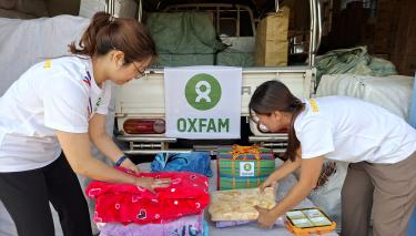 Zwei weiblich gelesene Personen in Oxfam-Shirts packen Kleidungsstücke und Handtücher zusammen.