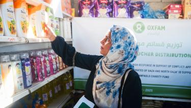 Eine Frau steht in einem Geschäft vor einem Regal, das mit Hygieneartikeln gefüllt ist. Im Hintergrund hängt ein Plakat mit der Aufschrift „Hygiene Voucher Distribution“ (Verteilung von Hygiene-Gutscheinen).