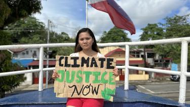 Eine Frau hält ein Plakat mit der Aufschrift  „Climate Justice Now“ (Klimagerechtigkeit jetzt).