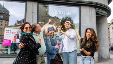 Fünf Personen stehen draußen vor dem Oxfam Shop in Halle und zeigen fröhlich auf das Logo.