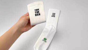 Tennissocken mit der Aufschrift „Tax the Rich“ (Reiche besteuern) und Oxfam. Eine in einer Hand, eine liegt.