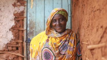 Madina Mohamed lebt in Isiolo County in Kenia, wo Oxfams Partnerorganisation MID-P die Wasserversorgung verbessert. Eine Frau lächelt in die Kamera. Sie lehnt an einer Wand, ihr Blick ist selbstsicher und stolz.