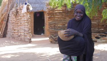 Ein Frau sitzt vor ihrem Haus und hält eine Schüssel in der Hand