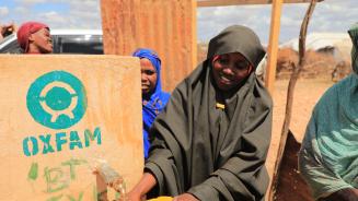 Mehrere Frauen stehen an einem von Oxfam errichteten Wassertank und füllen ihre Flaschen auf.