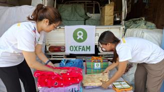 Zwei weiblich gelesene Personen in Oxfam-Shirts packen Kleidungsstücke und Handtücher zusammen.