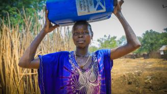 Eine Frau trägt einen Wasserkanister auf dem Kopf.
