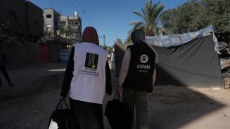 Zwei Frauen mit großen Taschen in Rückenansicht. Eine trägt eine Weste der Organisation Juzoor, die andere eine Weste von Oxfam.