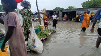 Menschen stehen auf einem überfluteten Marktplatz knöcheltief im braunen Wasser.