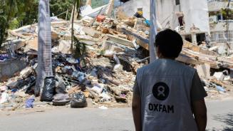 Eine Person in Oxfam-Weste. Im Hintergrund Trümmer.