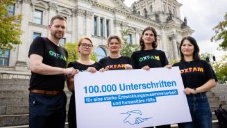 Fünf Personen stehen auf einer Treppe vor dem Bundestag und halten ein Schild mit der Aufschrift: 100.000 Unterschriften für eine starke Entwicklungszusammenarbeit und humanitäre Hilfe.