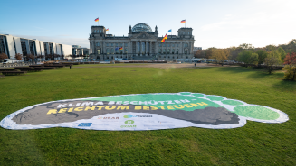 Überdemensionaler Fußabdruck als Tranparent auf der Wiese vor dem Reichstagsgebäude. Es trägt die Aufschrift "Klima beschützen - Reichtum bestuern"