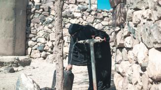 Haneen* (in schwarzem Gewand und mit Niqab bekleidet) dreht einen Wasserhahn vor ihrem Haus auf, um einen Wasserkanister zu befüllen.